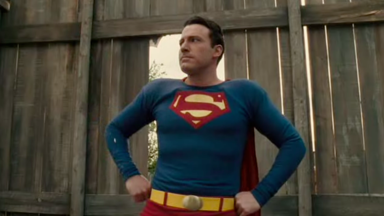 Ben Affleck as George Reeves as Superman in Hollywoodland, posing with fists on his hips, looking toward a brighter future in front of a wooden fence.