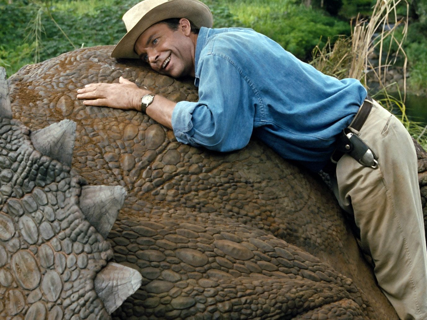 Jurassic Park: Dr. Grant smiles as he leans against a triceratops that is too big for him to hug.