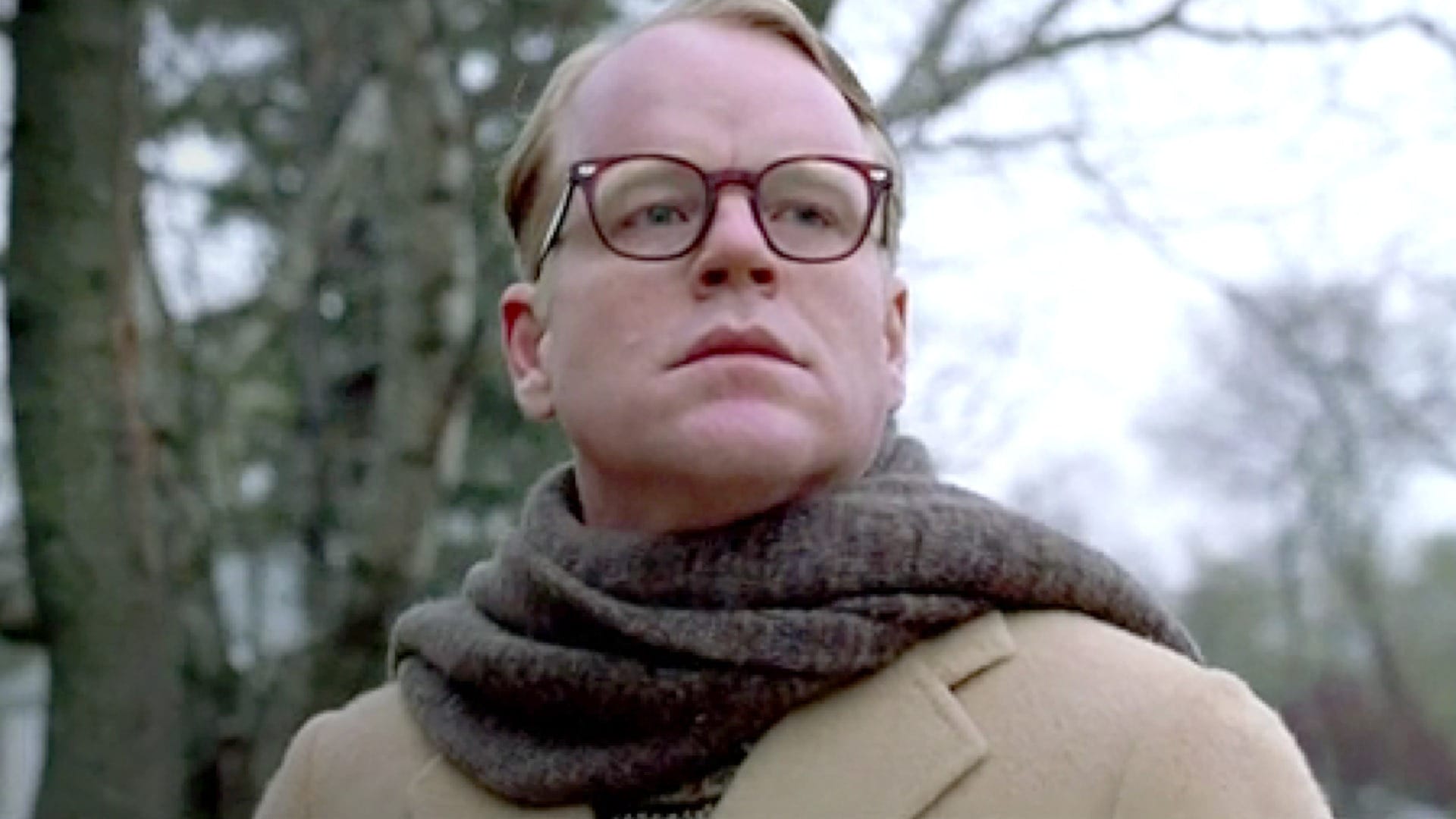 Capote: Philip Seymour Hoffman stands outside with a scarf and glasses, looking at something.