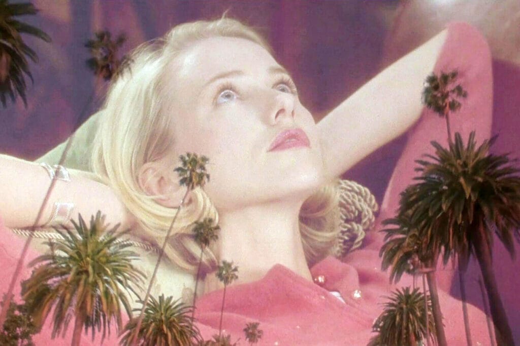 Mulholland Dr.: Betty lies back in a pink cardigan with a dreamy expression as palm trees superimpose over her.