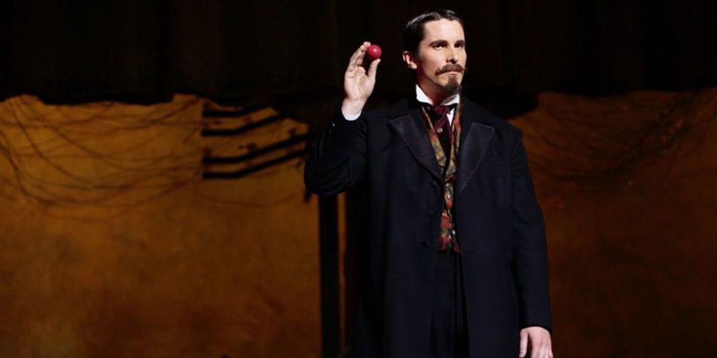 The Prestige: Borden stands on stage, holding up a red ball to the audience to draw their attention.
