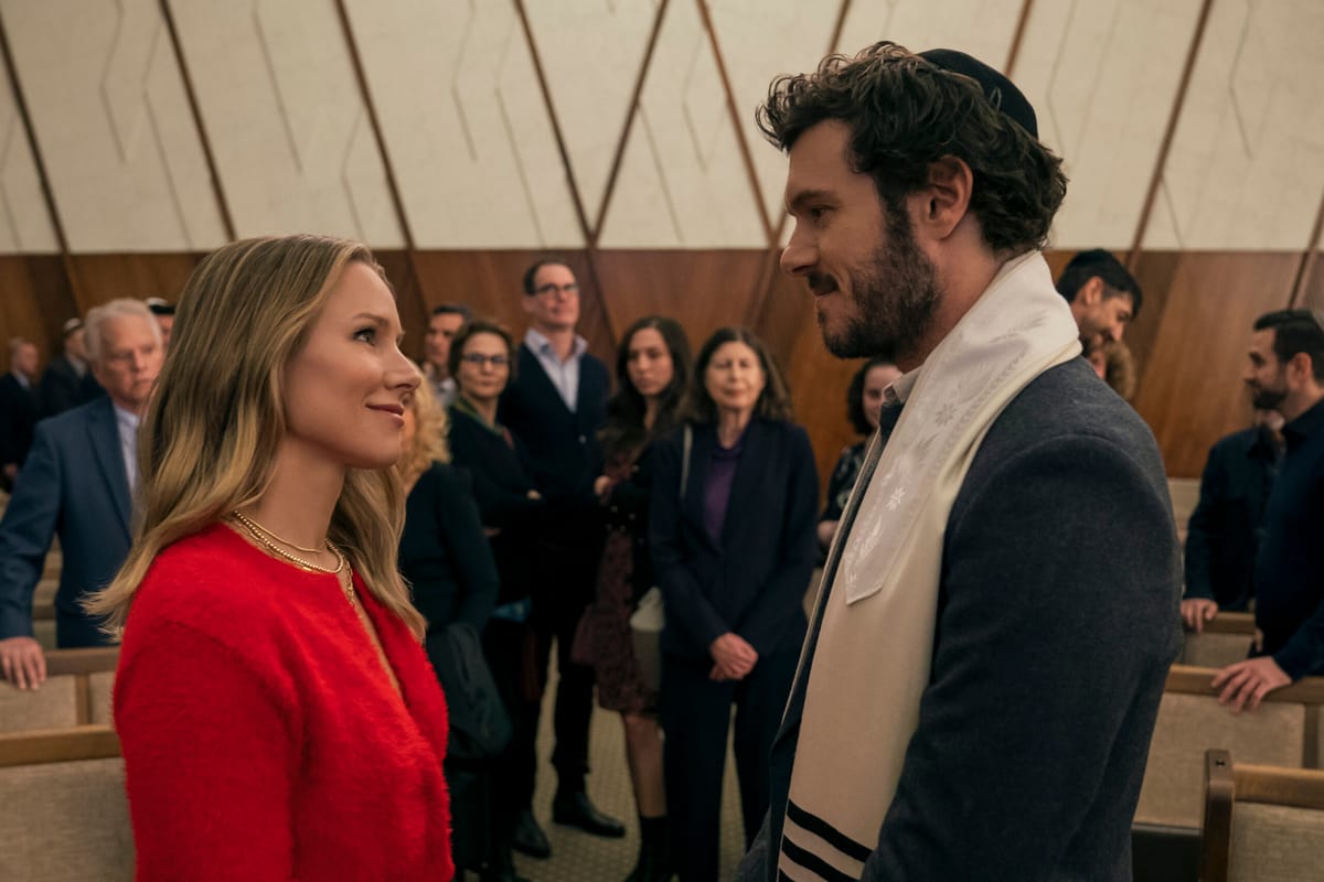 A blonde woman in a red sweater is making eye contact with a tall, attractive Rabbi in a still from Nobody Wants This