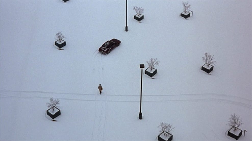 An overhead shot of a man walking to his car in a snowy parking lot