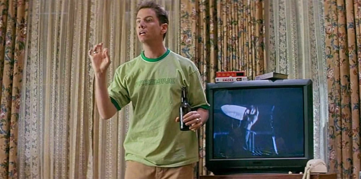 Shot from Scream with Jamie Kennedy standing next to a paused TV showing a slasher movie as he explains the rules of the genre.