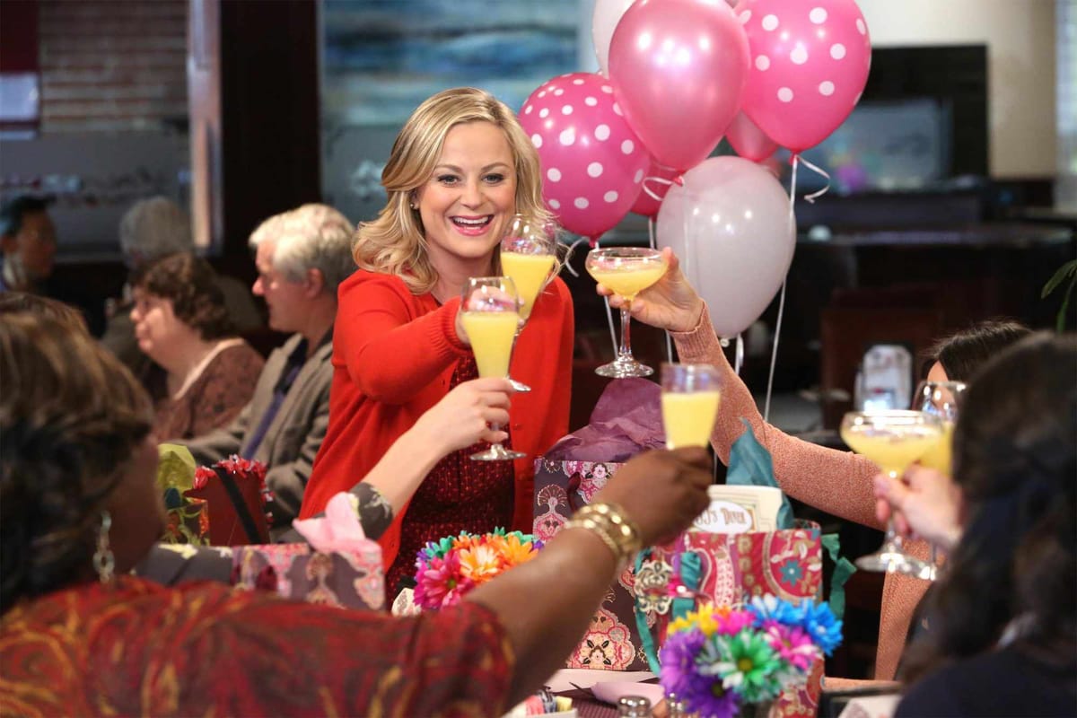 Leslie Knope and friends at a restaurant, toasting with mimosas.