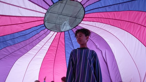 A young boy stands under a purple, white, pink and blue parachute in a still from I Saw the TV Glow