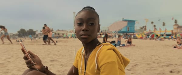 A young girl sits on the beach holding her phone in a still from Jordan Peele'Us.