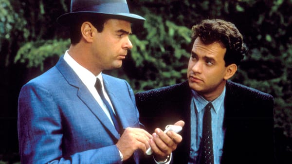 Dan Ackroyd and Tom Hanks in suits, looking at each other. Ackroyd holds a pocket-sized notebook. From Dragnet: The Movie.