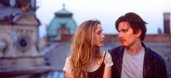 Julie Delpy and Ethan Hawke look into each other's eyes with Vienna in the background. Before Sunrise