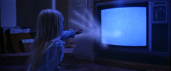 A little girl reaches out to touch a ghostly hand coming out of a TV in a still from Poltergeist