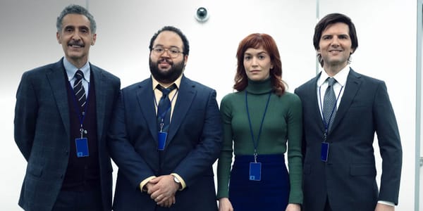 The Innies of Severance taking a group photo in the office with a security camera behind them.