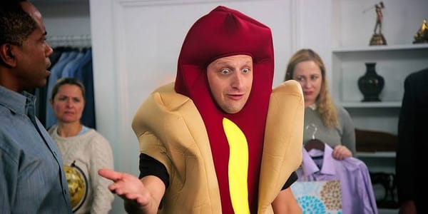 Tim Robinson in a Hot Dog Suit, trying to convince a room of people that the hot dog shaped car isn't his.