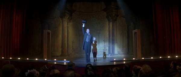 The Prestige: Angier stands on stage with his assistant, holding up a top hat before taking a bow.