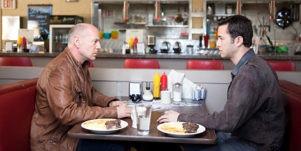Bruce Willis sits across from a young Bruce Willis in a still from Looper