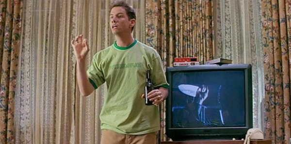 Shot from Scream with Jamie Kennedy standing next to a paused TV showing a slasher movie as he explains the rules of the genre.