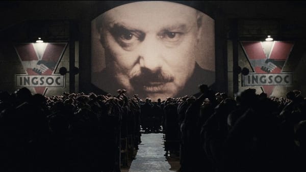 Screencap 1984: A giant image of Big Brother looks down on an assembled crowd. Large INGSOC banners hang on either side of the monitor.